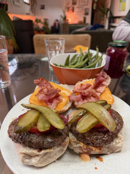 This photo captures a cozy indoor meal featuring homemade burgers with various toppings and a side of green beans, likely enjoyed at a home in Oudeschans, Uilenburg, Amsterdam